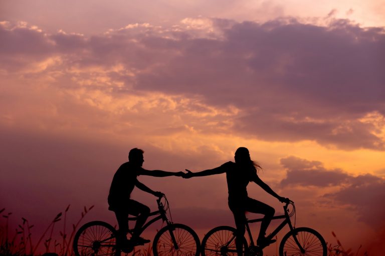 two people in bicycles, front person reaching out hand to person behind them